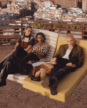 Four people posing together on a bench with a cityscape in the background, holding the Marshall Emberton II.