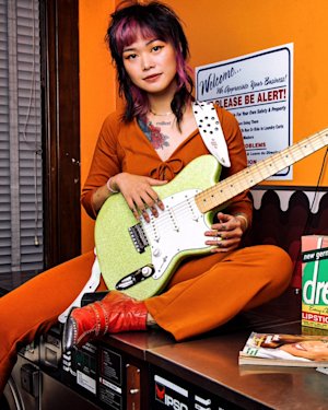 A girl sitting on top of a desk and holding a guitar.