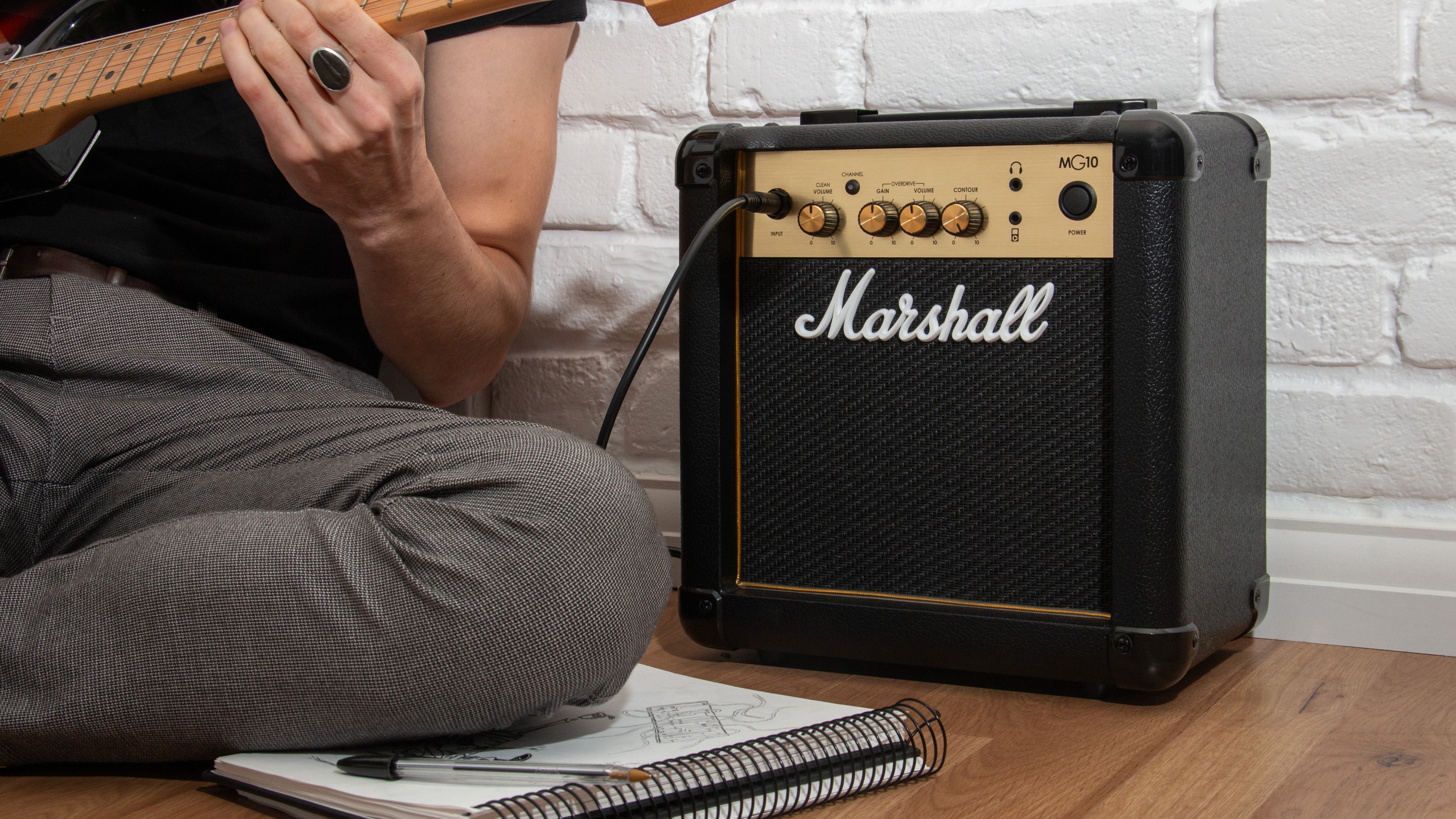 Un hombre toca una guitarra eléctrica junto a un amplificador Marshall MG10.