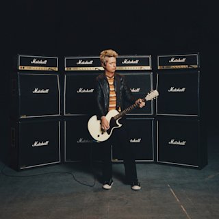 Billie Joe Armstrong posing for a photo whilst playing a guitar connected to Marshall amplifiers in a studio.