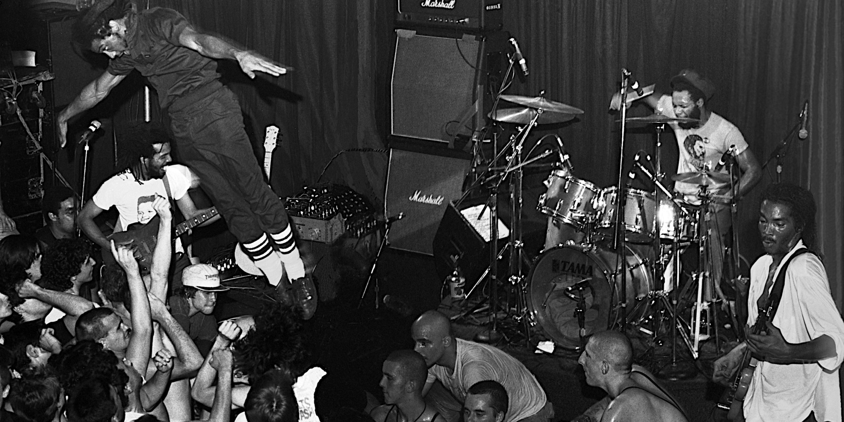 Schwarz-Weiß-Foto eines Musikers, der mit Marshall-Verstärkern auf der Bühne in die Menge springt.