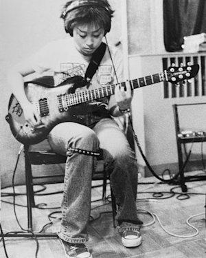 Gia Wang vocalist in Hang On The Box sat on a chair playing an electric guitar