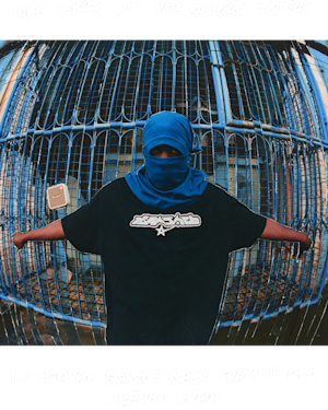 Kelvin Krash wearing a blue balaclava and posing in front of a blue metal fence.
