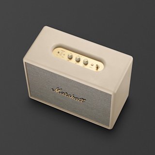 A Marshall Woburn III Bluetooth speaker in cream with brass control knobs, placed on a dark gray surface.