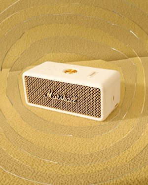 Marshall Emberton III Cream bluetooth portable speaker with a mesh front on a textured yellow surface.