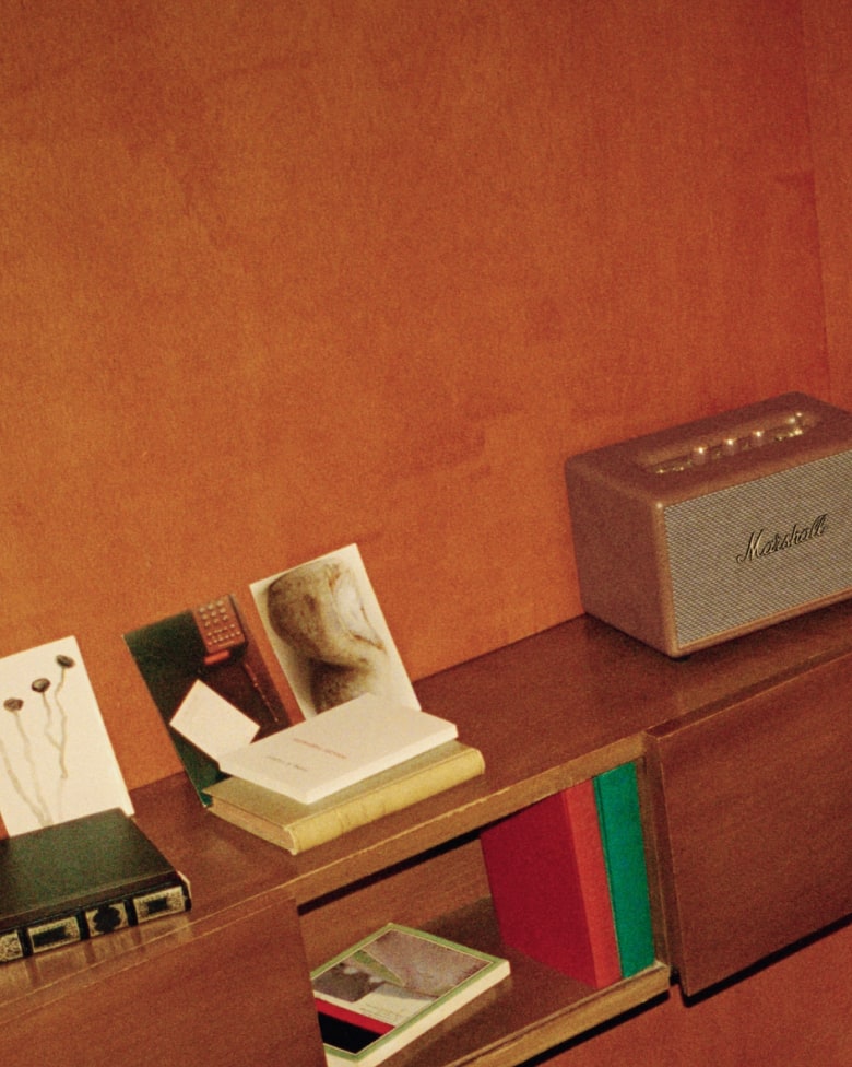 A brown Stanmore III speaker standing on a teak bookshelf