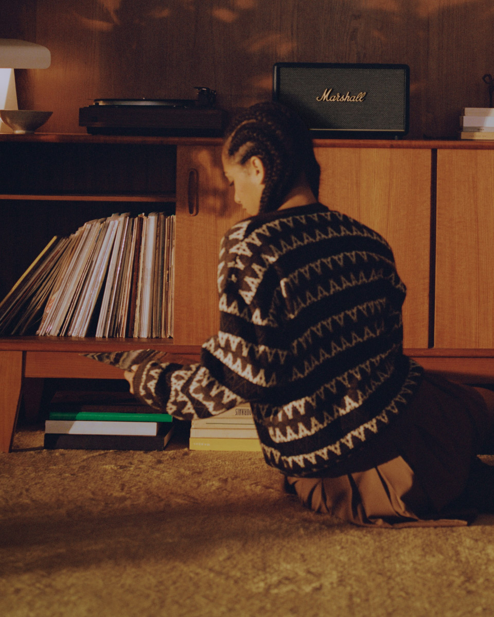 Ein Mädchen sitzt auf dem Boden und schaut sich ihre Vinyls an, während sie einen Marshall Black Speaker hört.
