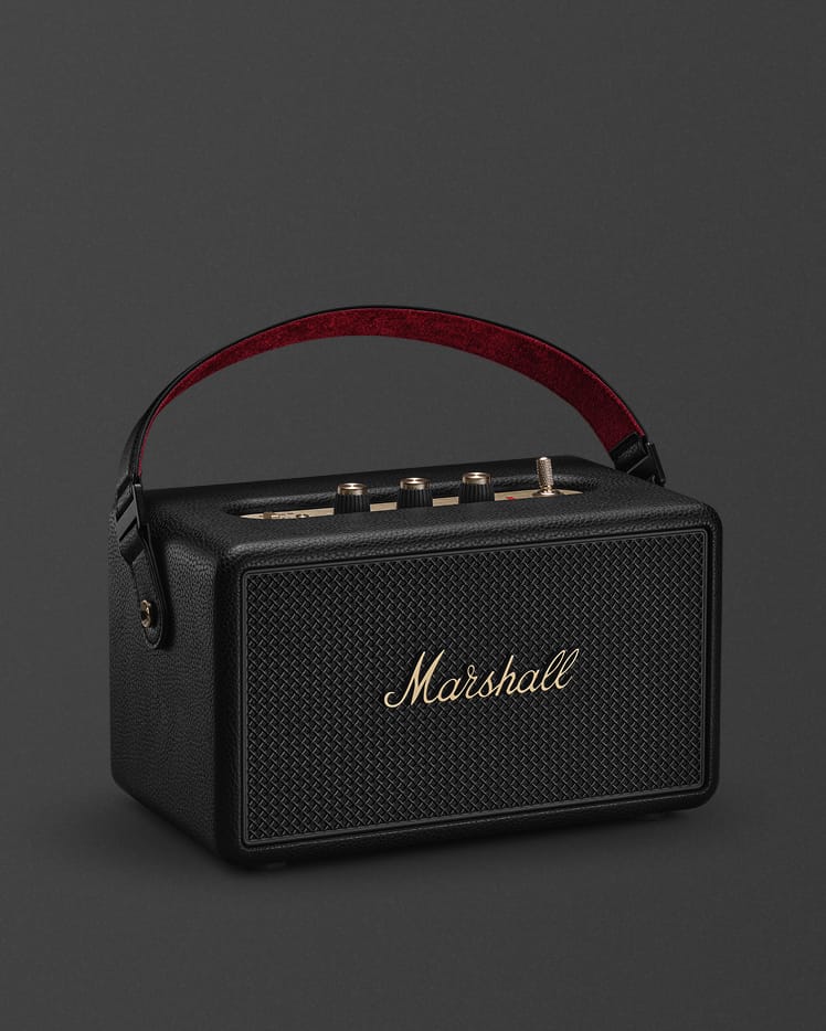 The Marshall Kilburn III Black and Brass portable bluetooth speaker with a red-lined handle and gold control knobs on top.