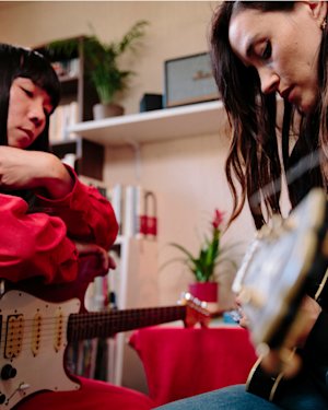 Yuki Tsujii sitting and Theresa Wayman playing a guitar in the room.