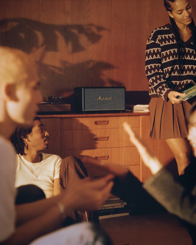 A group of people sitting in a room listening to music through a Marshall Stanmore III, a black Marshall speaker.