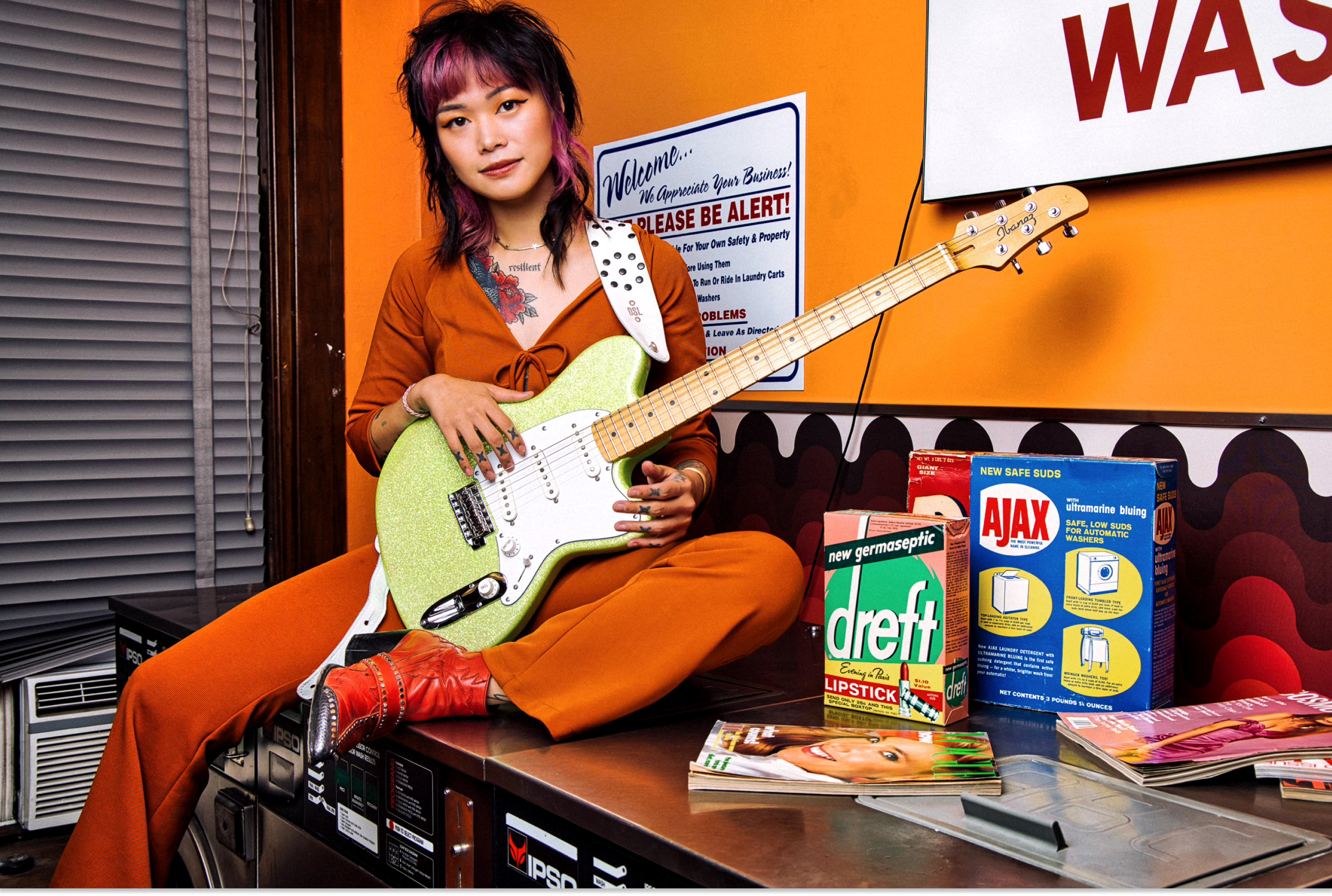 Yvette Young sat on top of a washing machine holding her guitar in a laundrette