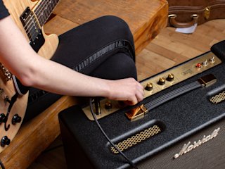 Imagen de cerca del guitarrista con una guitarra beige sentado y girando el Marshall Origin50 Combo