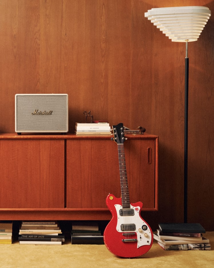 A red guitar sitting in front of a Marshall Woburn III Cream.