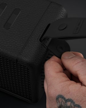 A hand with tattoos attaching the carry strap on a Middleton speaker.