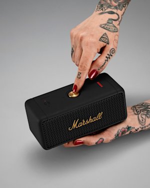 A pair of hands with tattoos holding an Emberton speaker and pushing the Control knob on top of it.