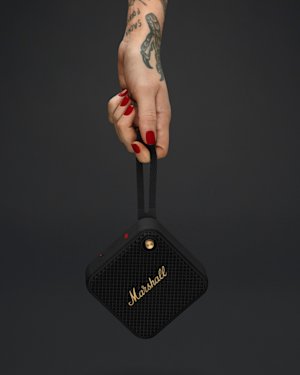 A hand with tattoos holding a Willen speaker in its strap.