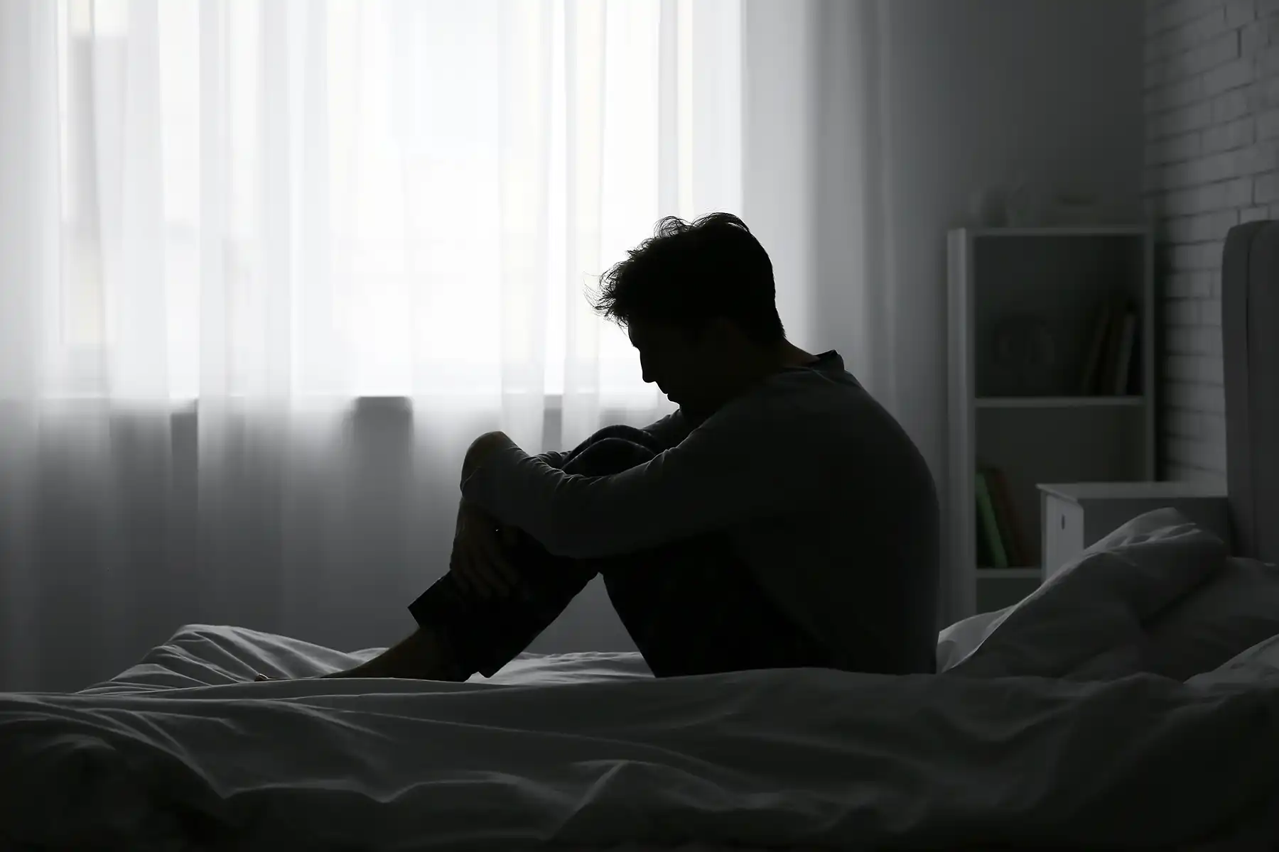 Depressed man sitting on his bed in the dark