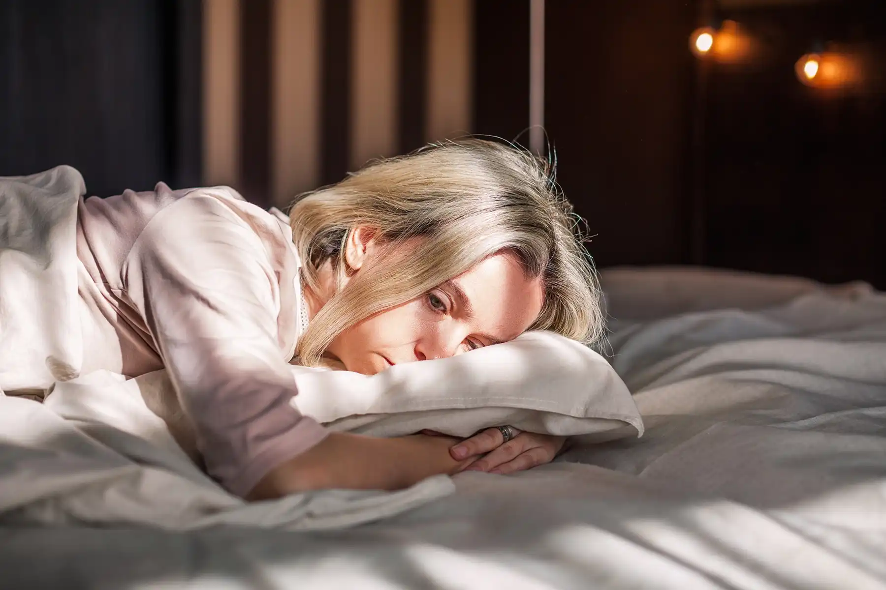 Image of a woman in bed sadly, hugging her pillow