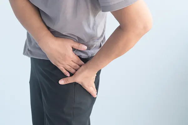 A man in a grey t-shirt and dark pants holds his hands to his left hip in pain.