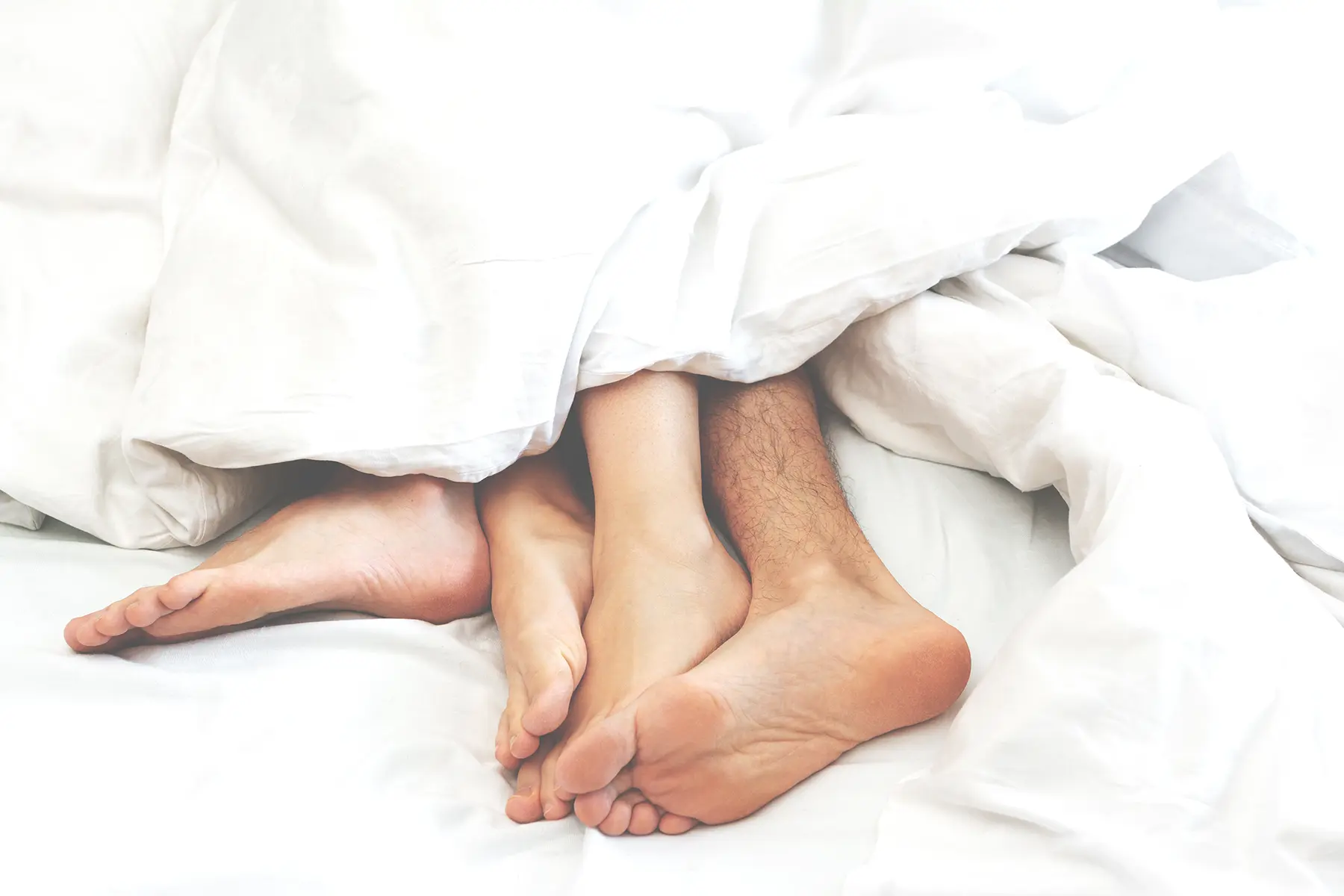 Male and female feet intertwined on the edge of a bed