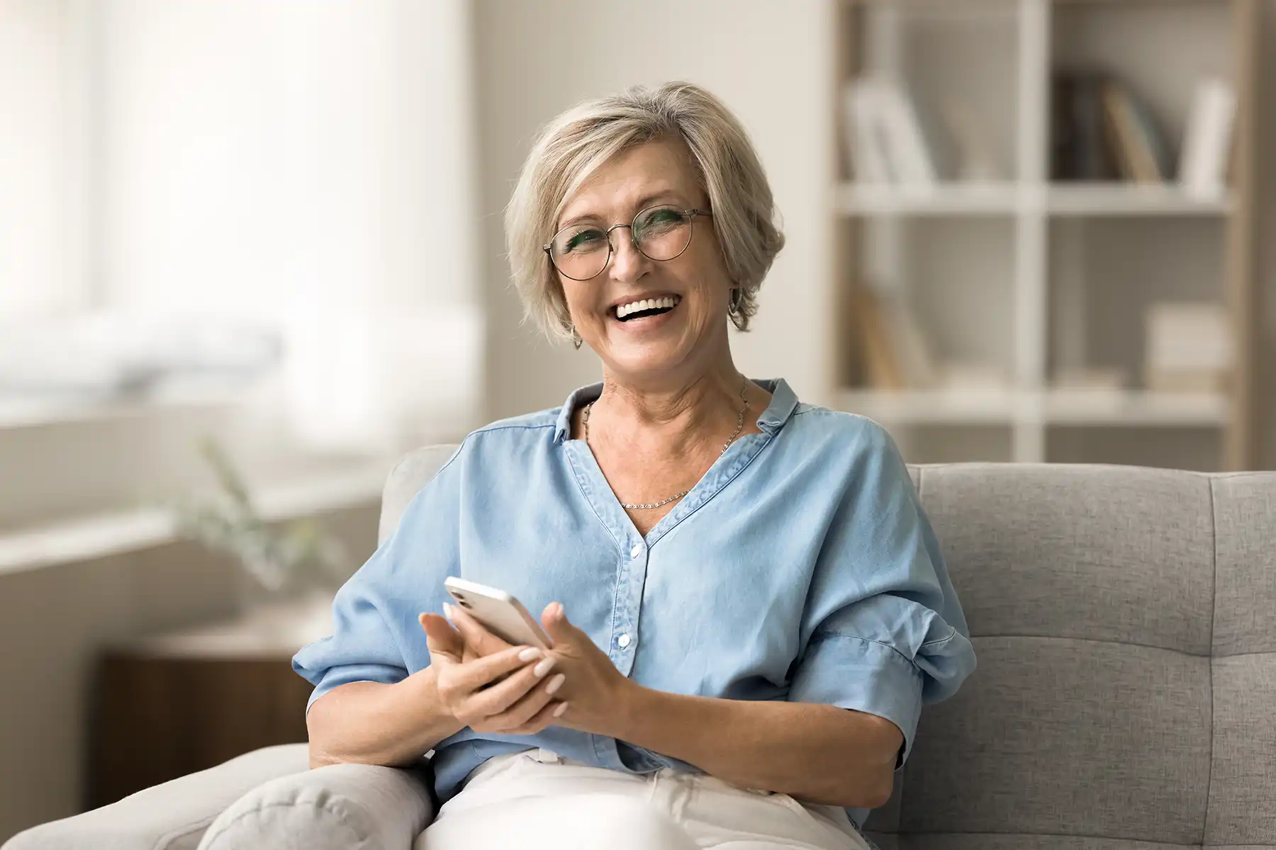 Older woman sitting on couch smiling with her phone in her hand.