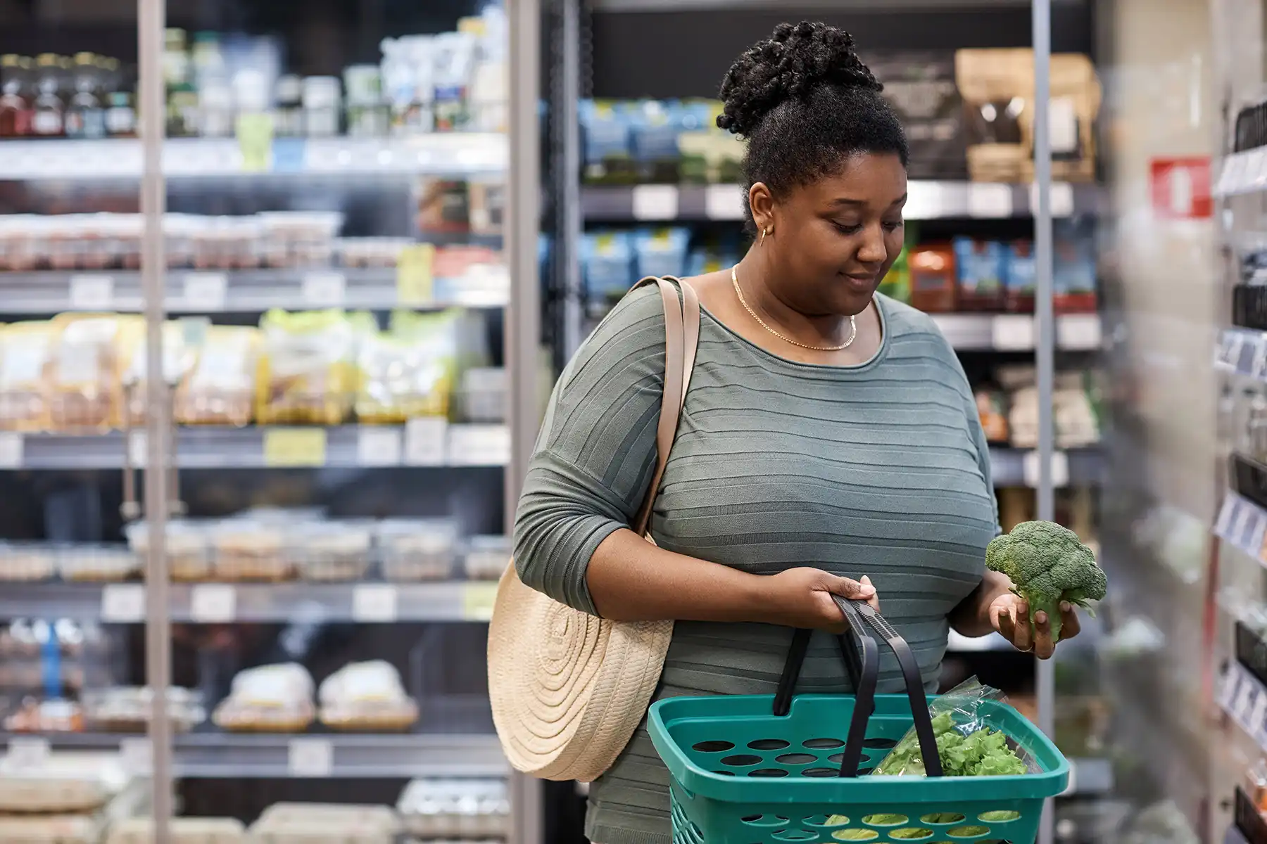 Woman at the grocery store putting broccoli in her cart.