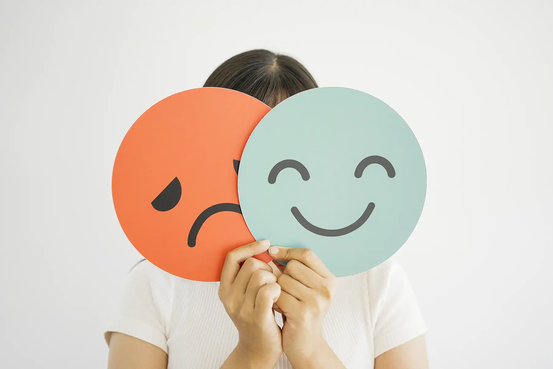 woman holding up a smiley face and a frowny face