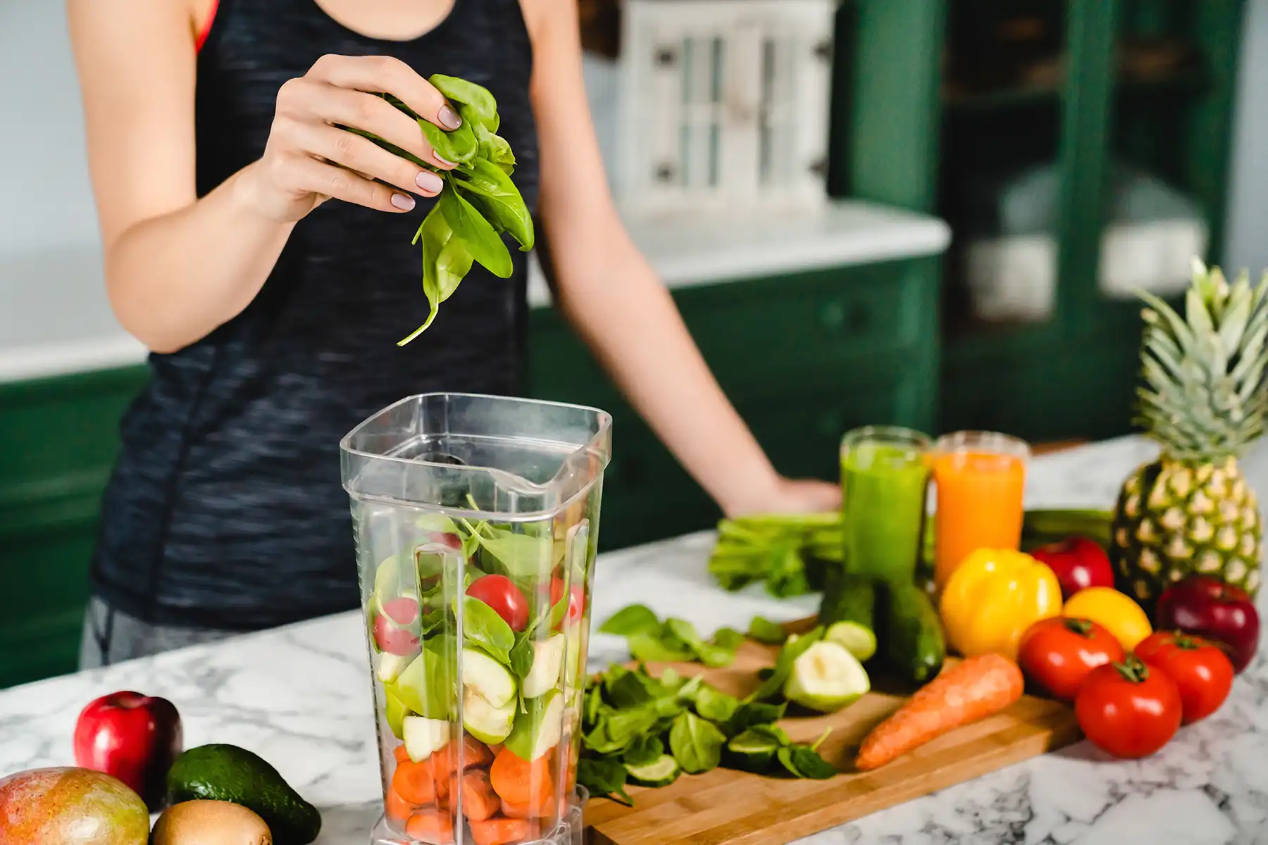 woman putting a variety of fruits and veggies in a blender