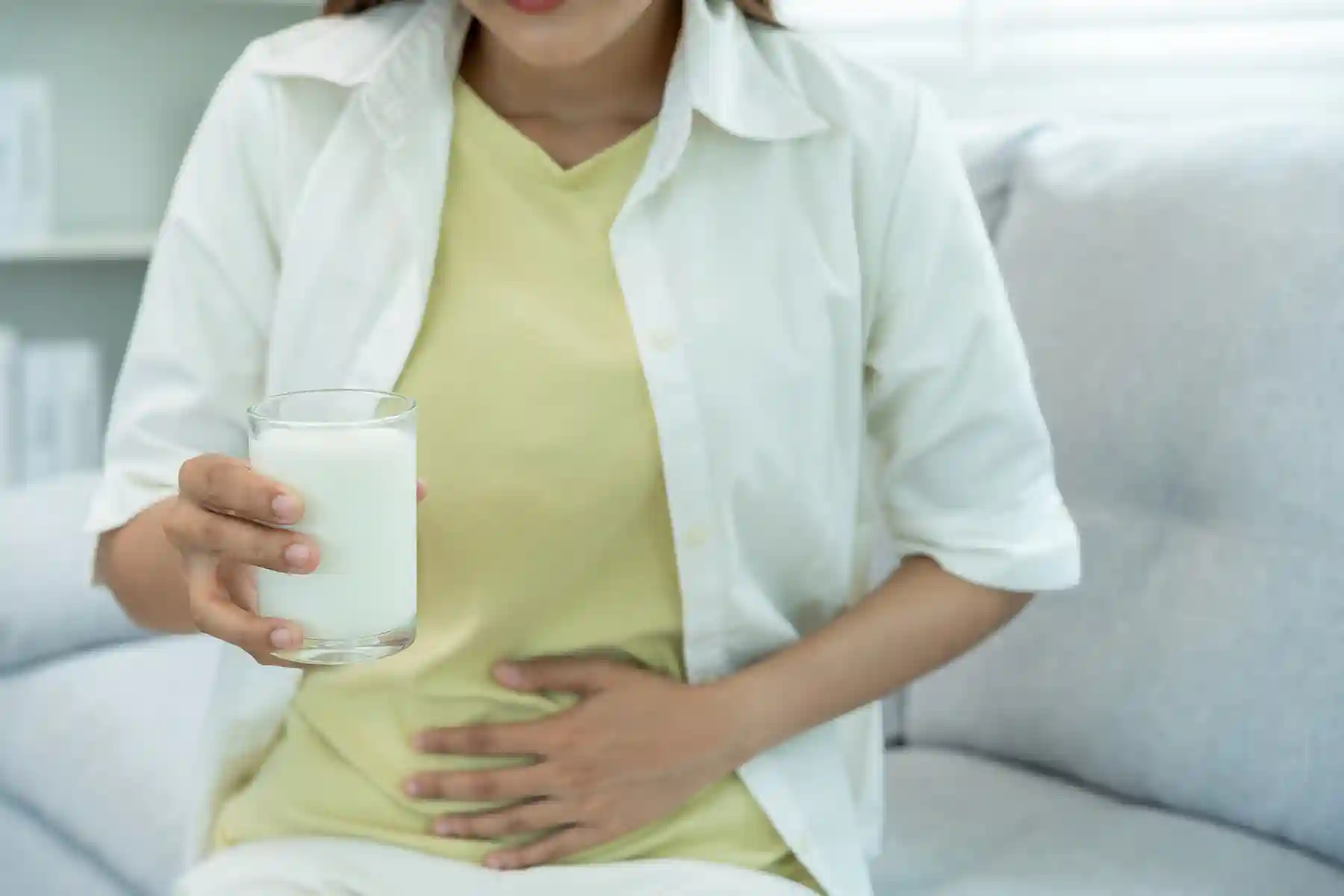 A woman holding a glass of milk while sitting in pain.