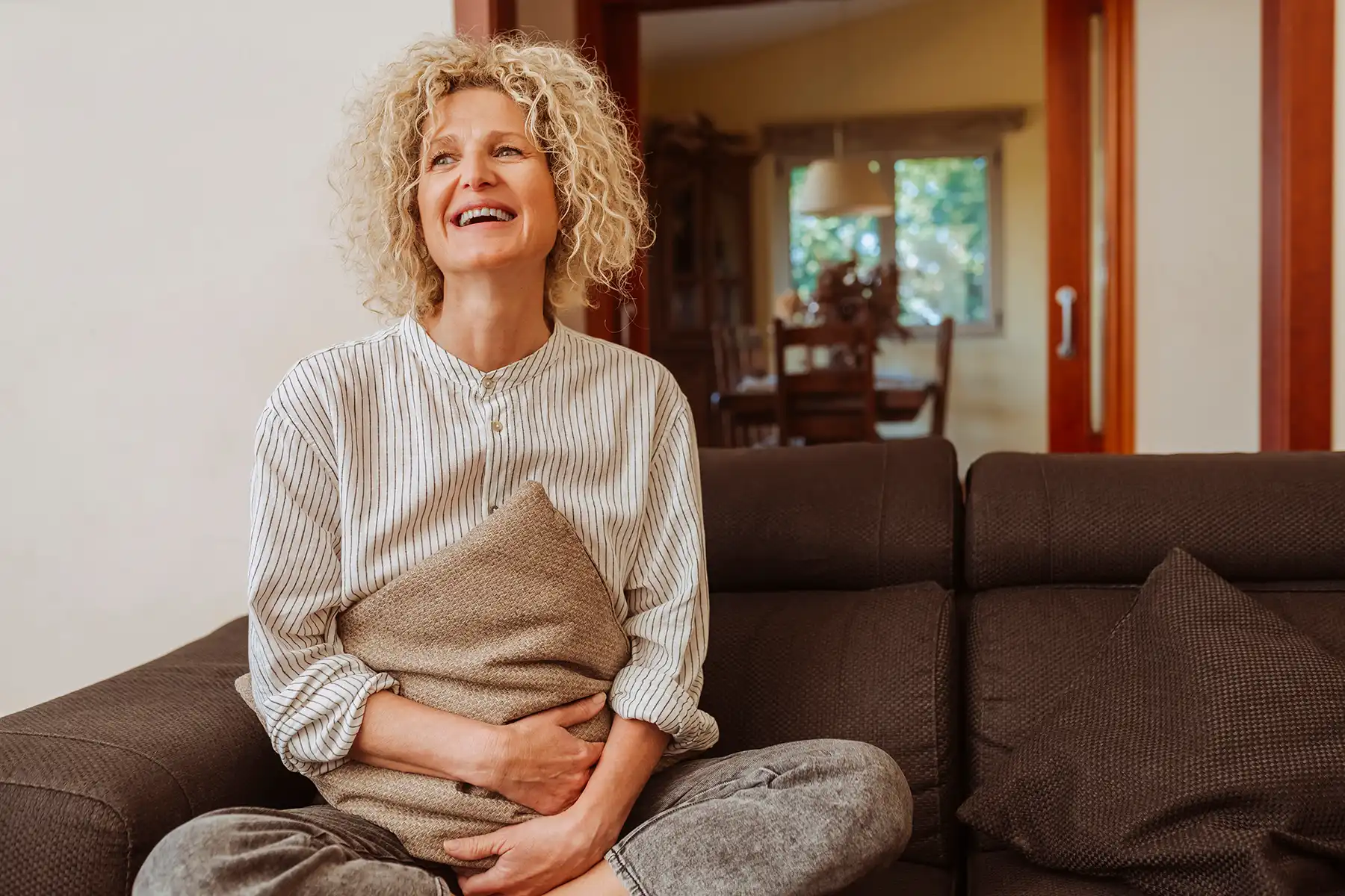Woman in her 50s smiling happily on her couch.