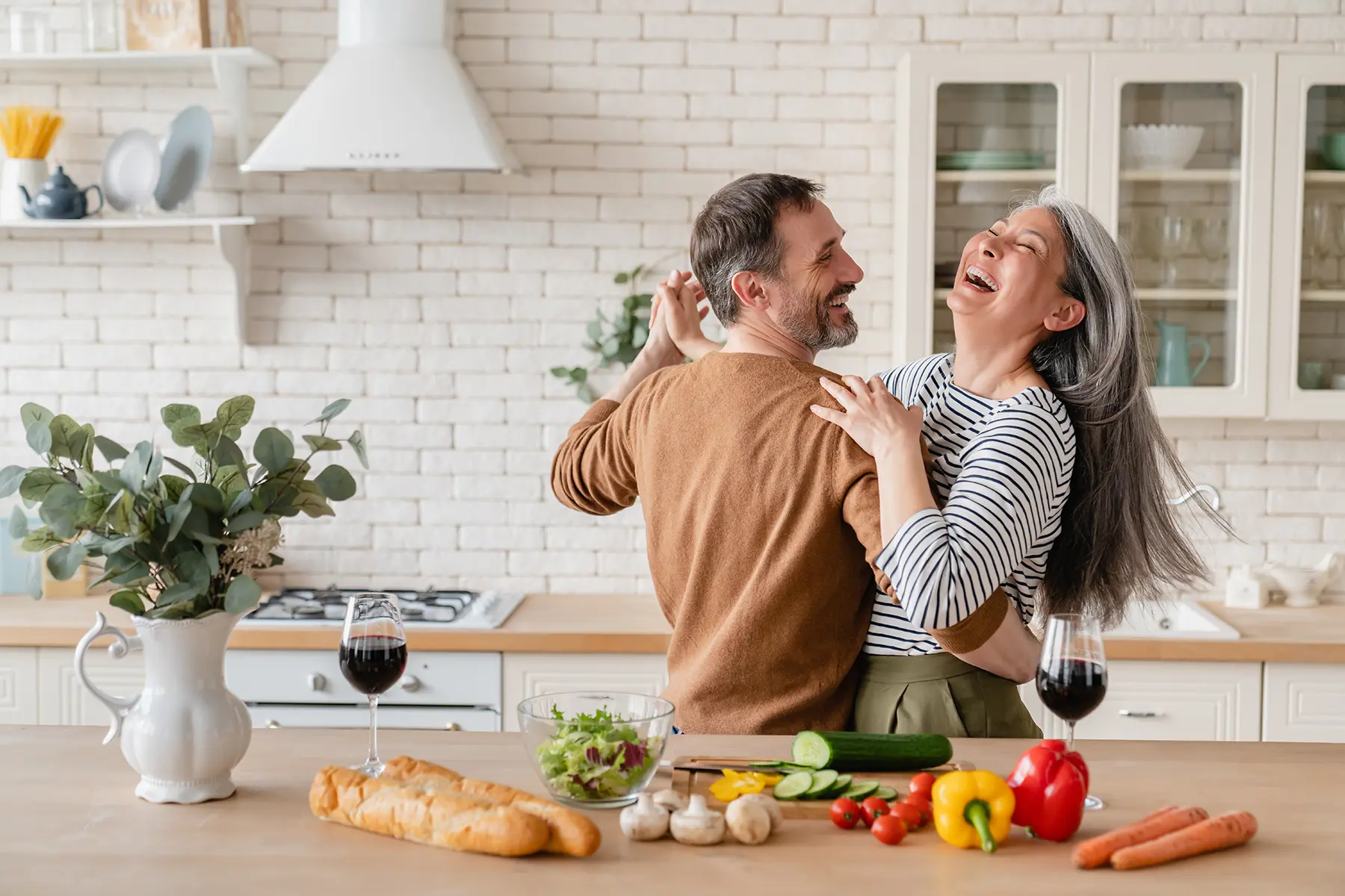 Happy middle aged couple dancing happily while cooking dinner