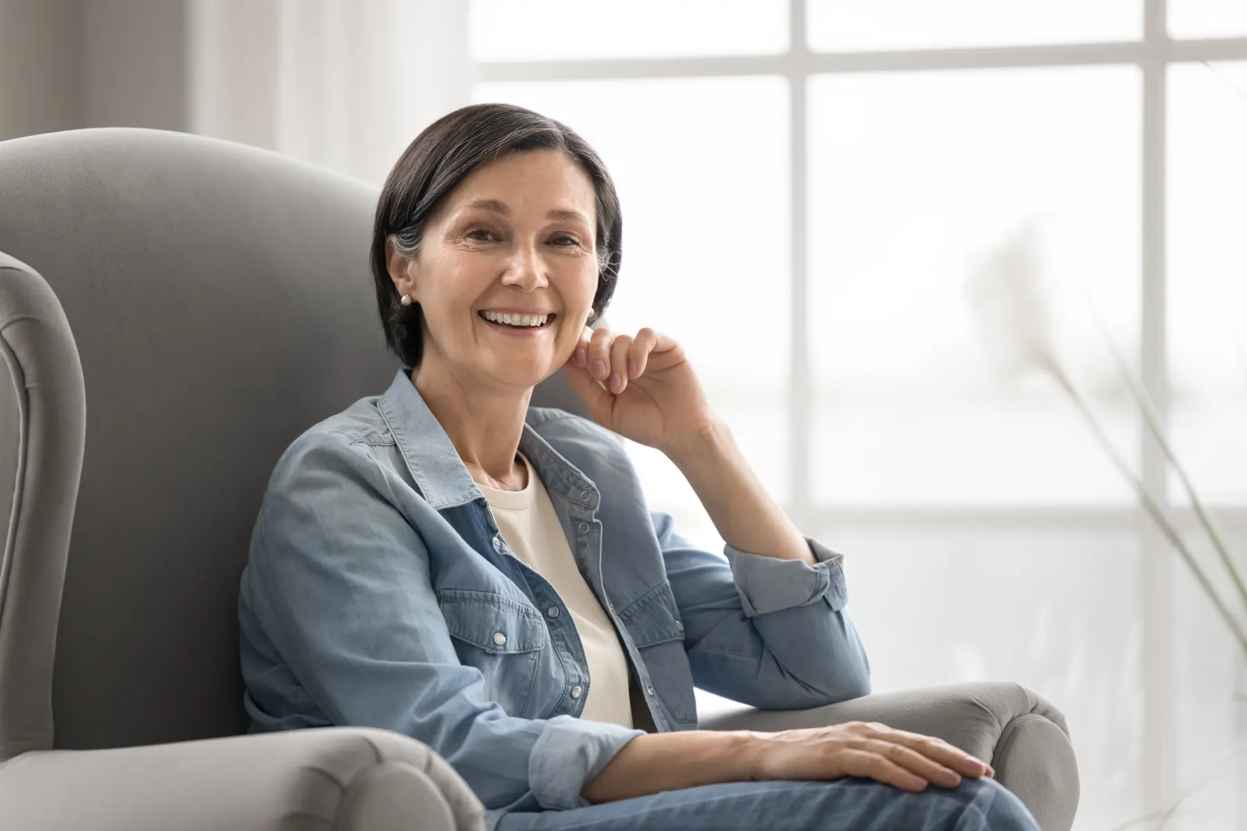Women in midlife sitting on couch with big smile on her face.