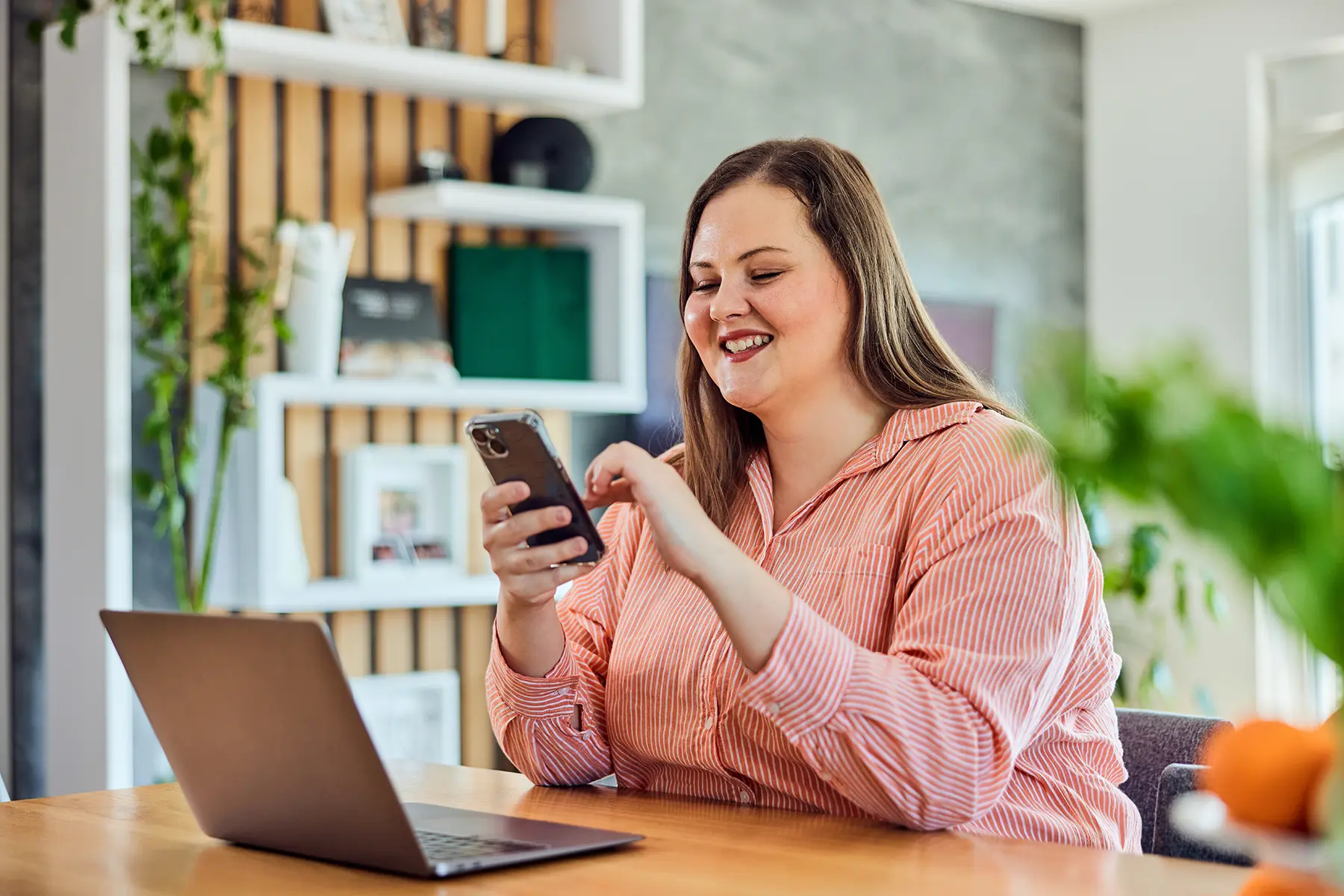Woman holding her mobile phone during work over the laptop, at home.