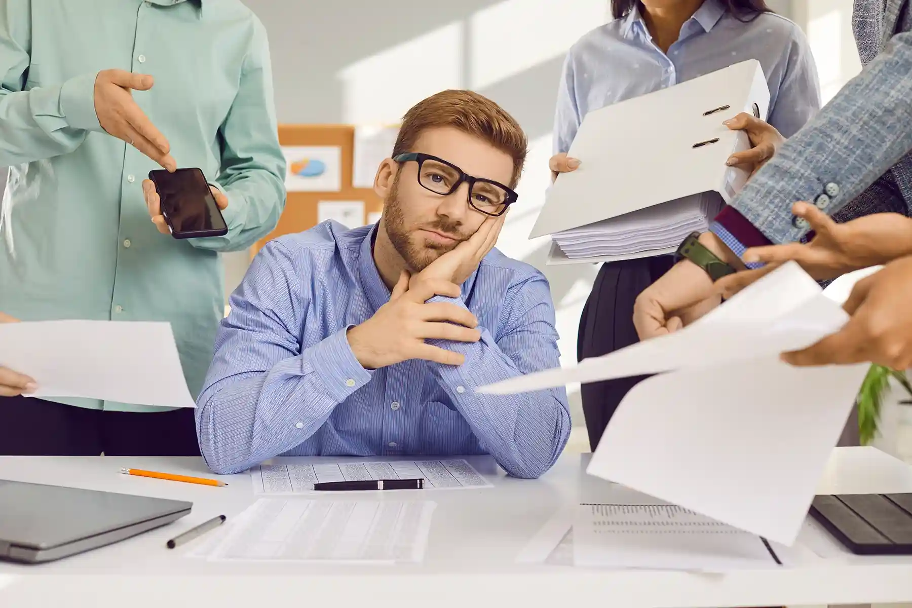 An image of a man in an office with several other employees assigning him tasks to handle.