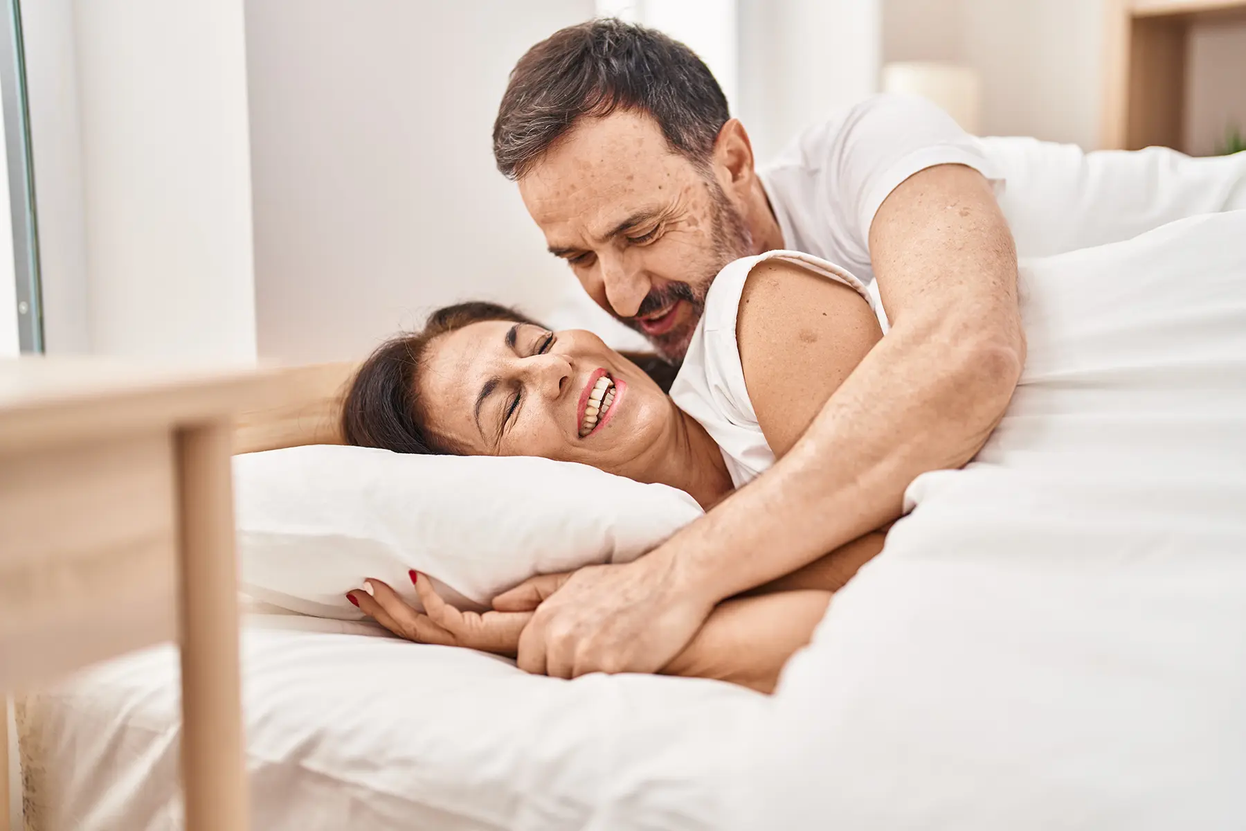 Middle aged couple smiling and cuddling in bed