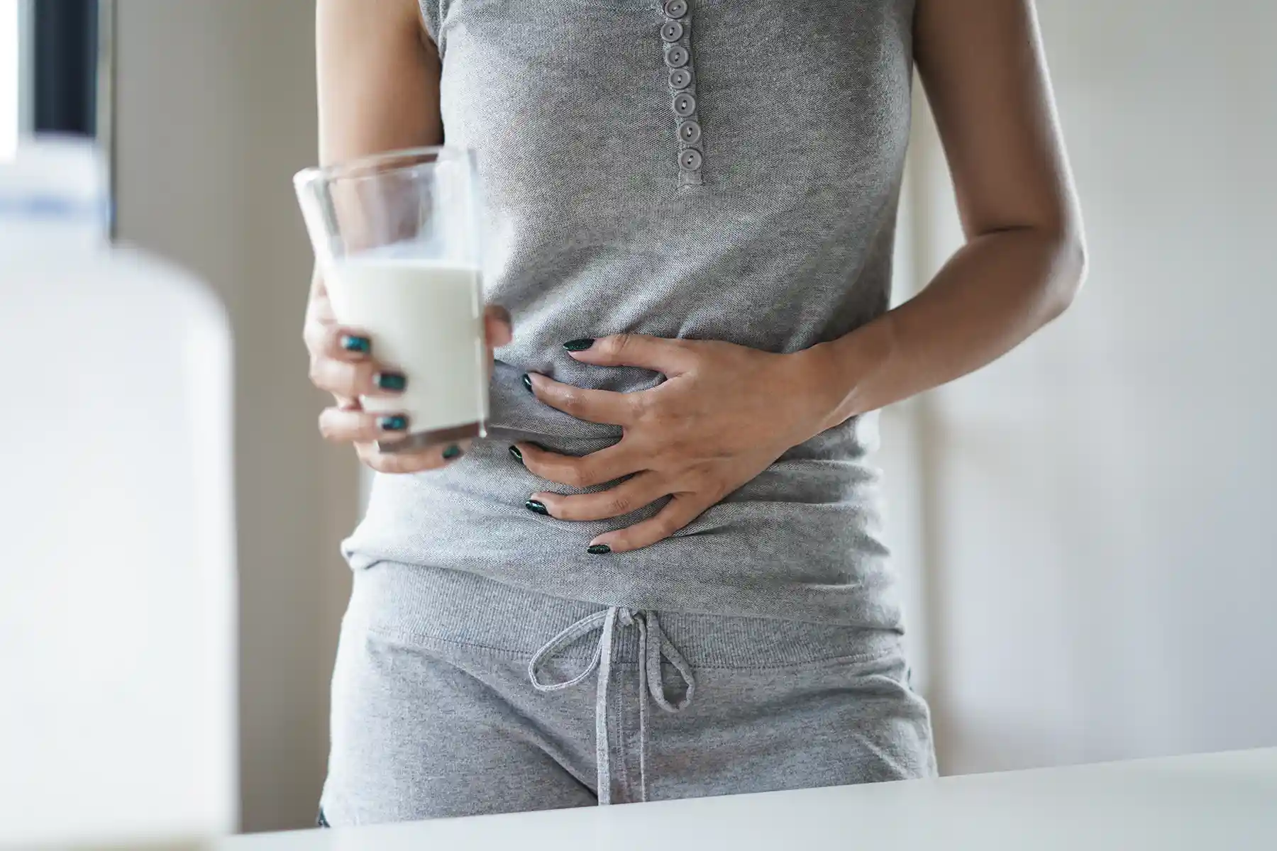 A woman holding her stomach in pain after drinking a glass of milk.