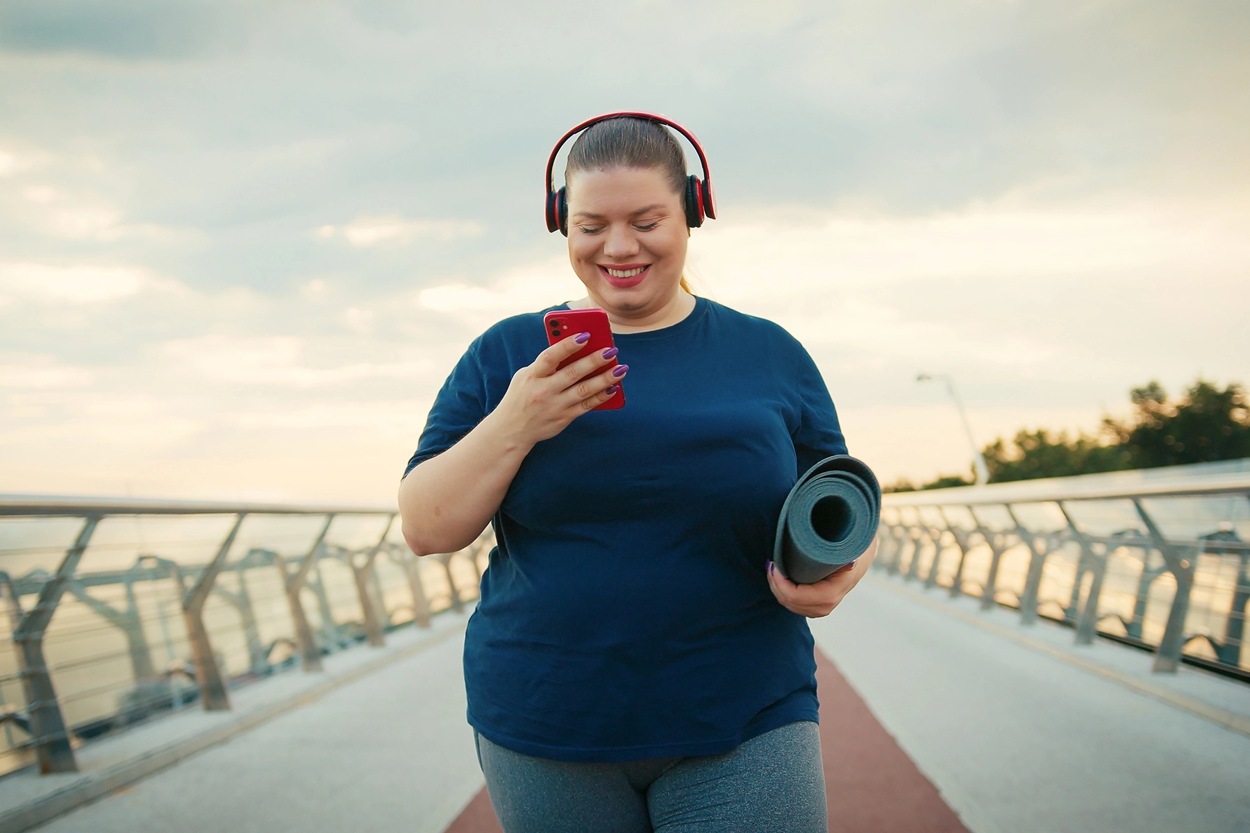 Woman on her way to do yoga outside while smiling at her phone