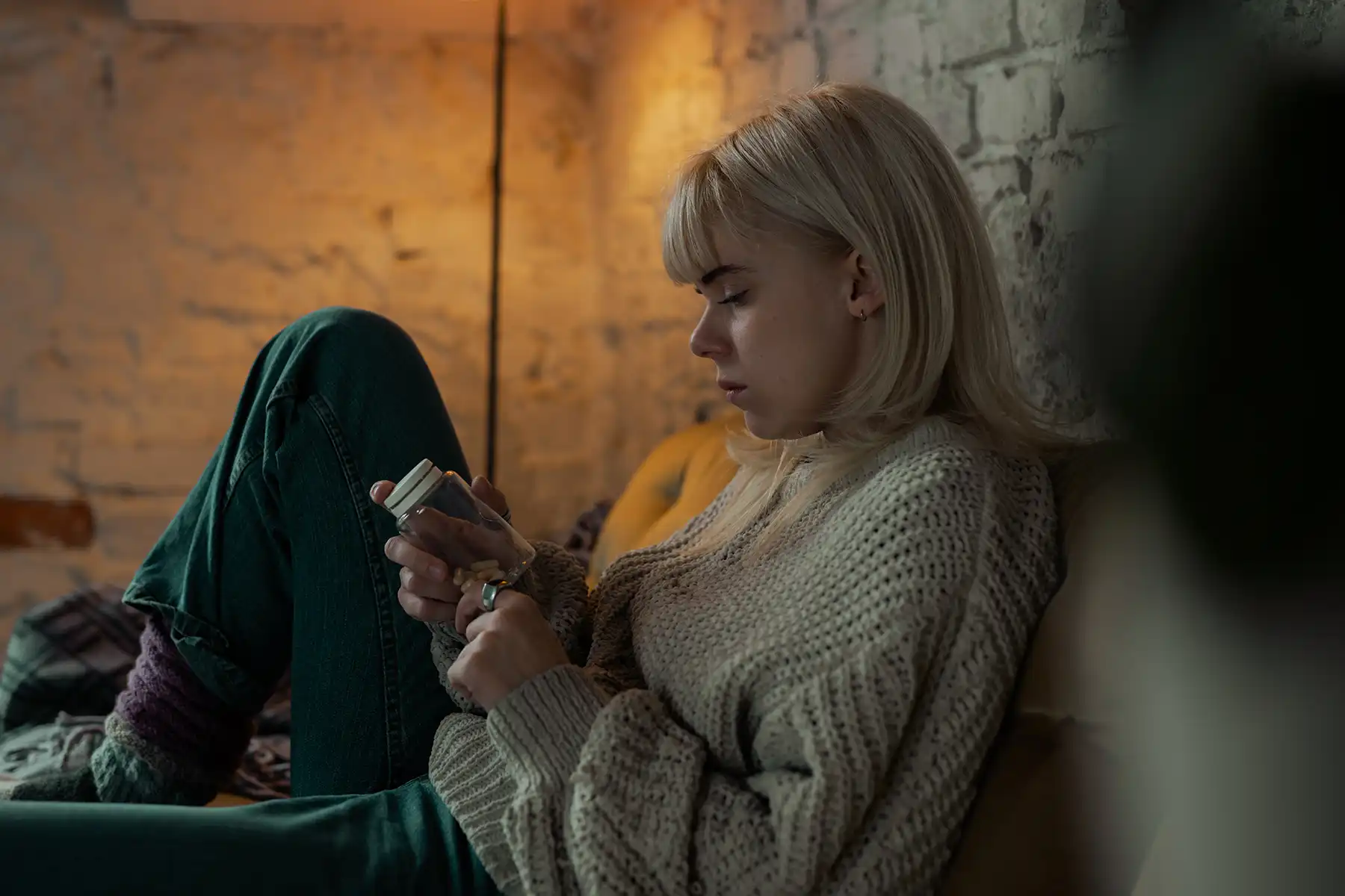 Woman sitting in the dark reading a pill bottle