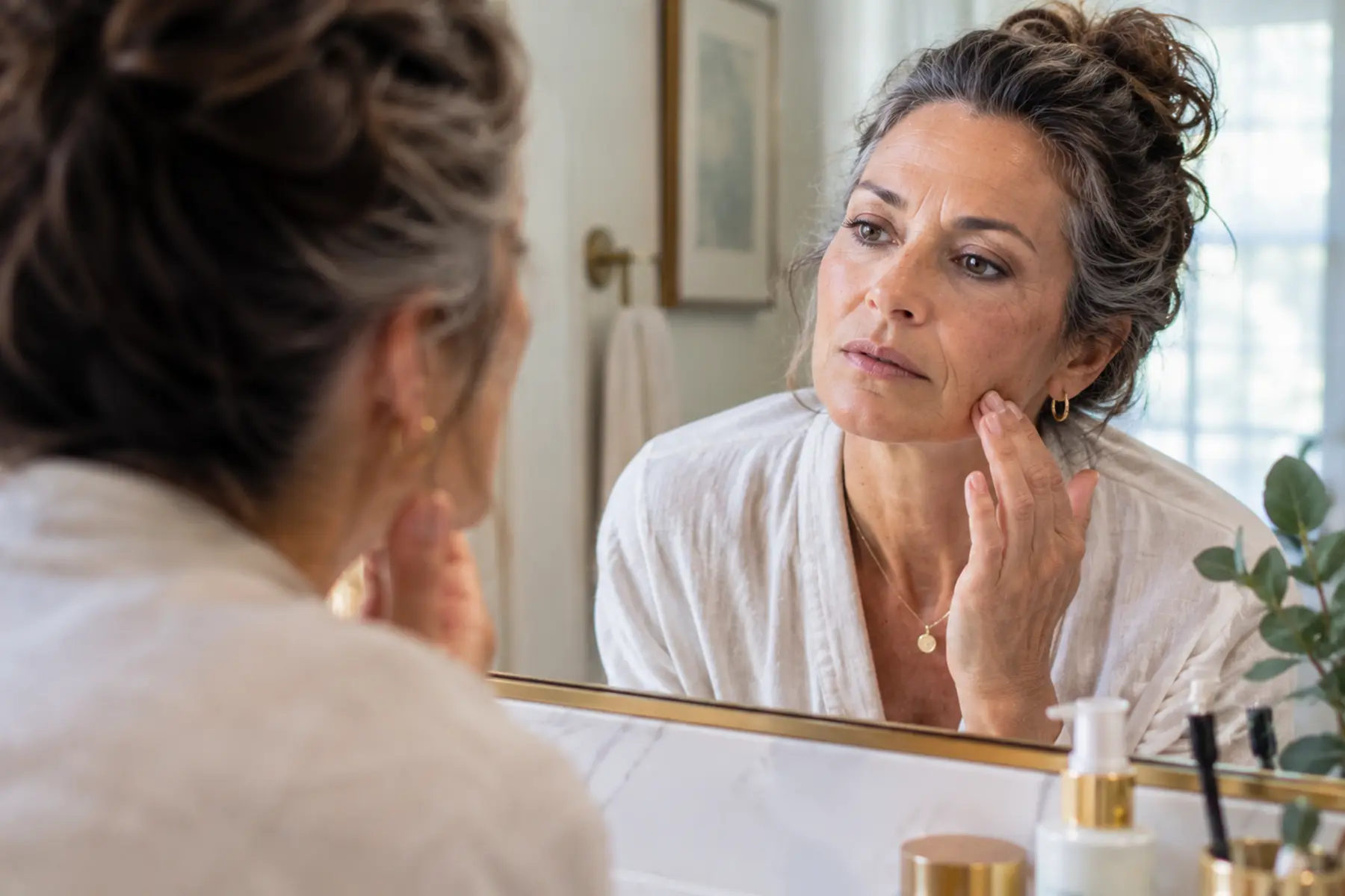 Woman in midlife looking at her face in the mirror