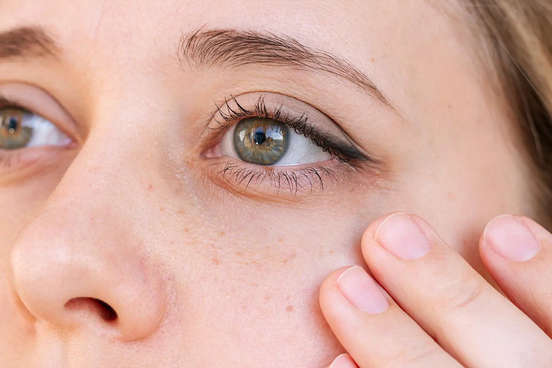 Close-up of a woman with her hands near one of her eyes.