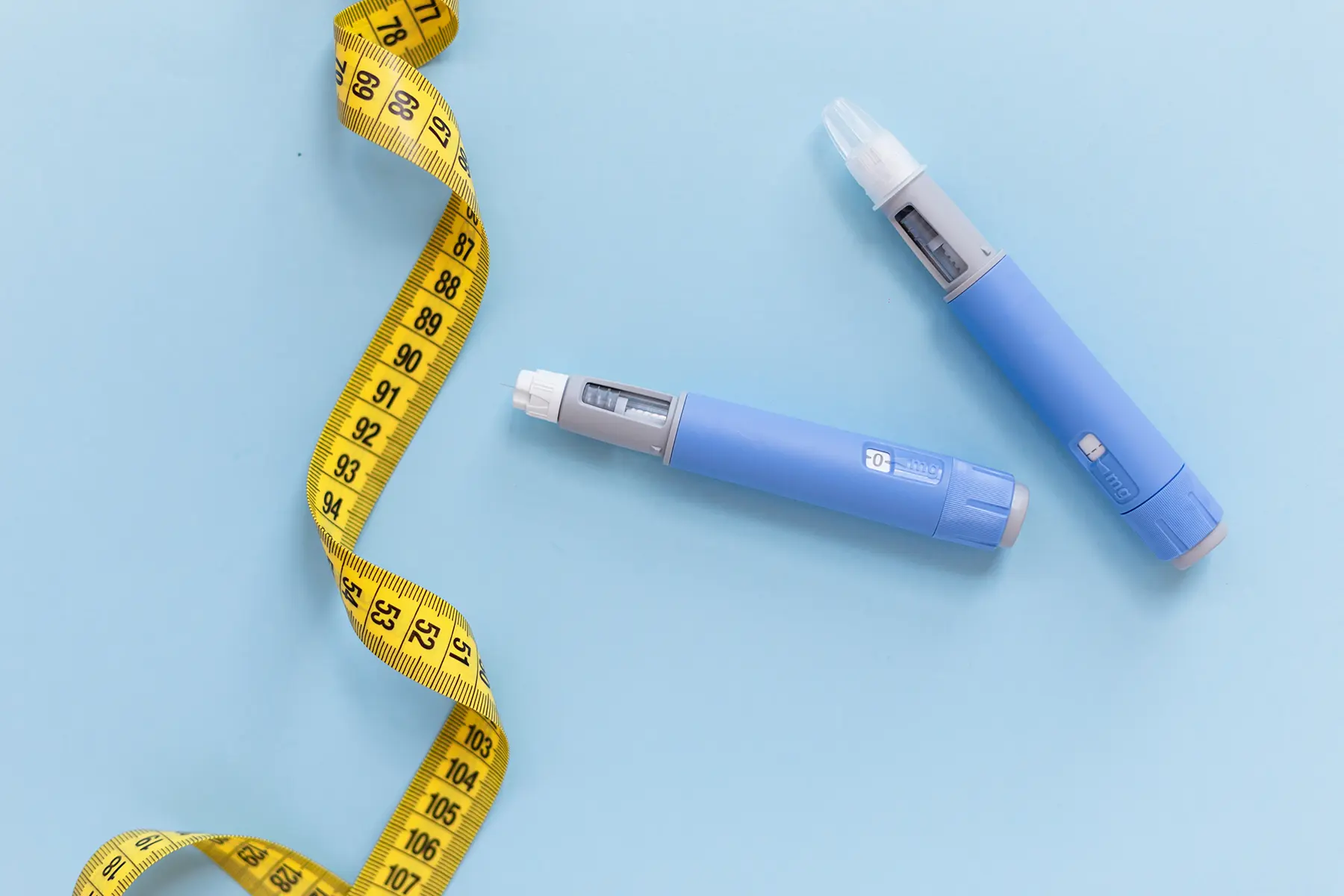 2 GLP-1 pens next to a twirled tape measure.