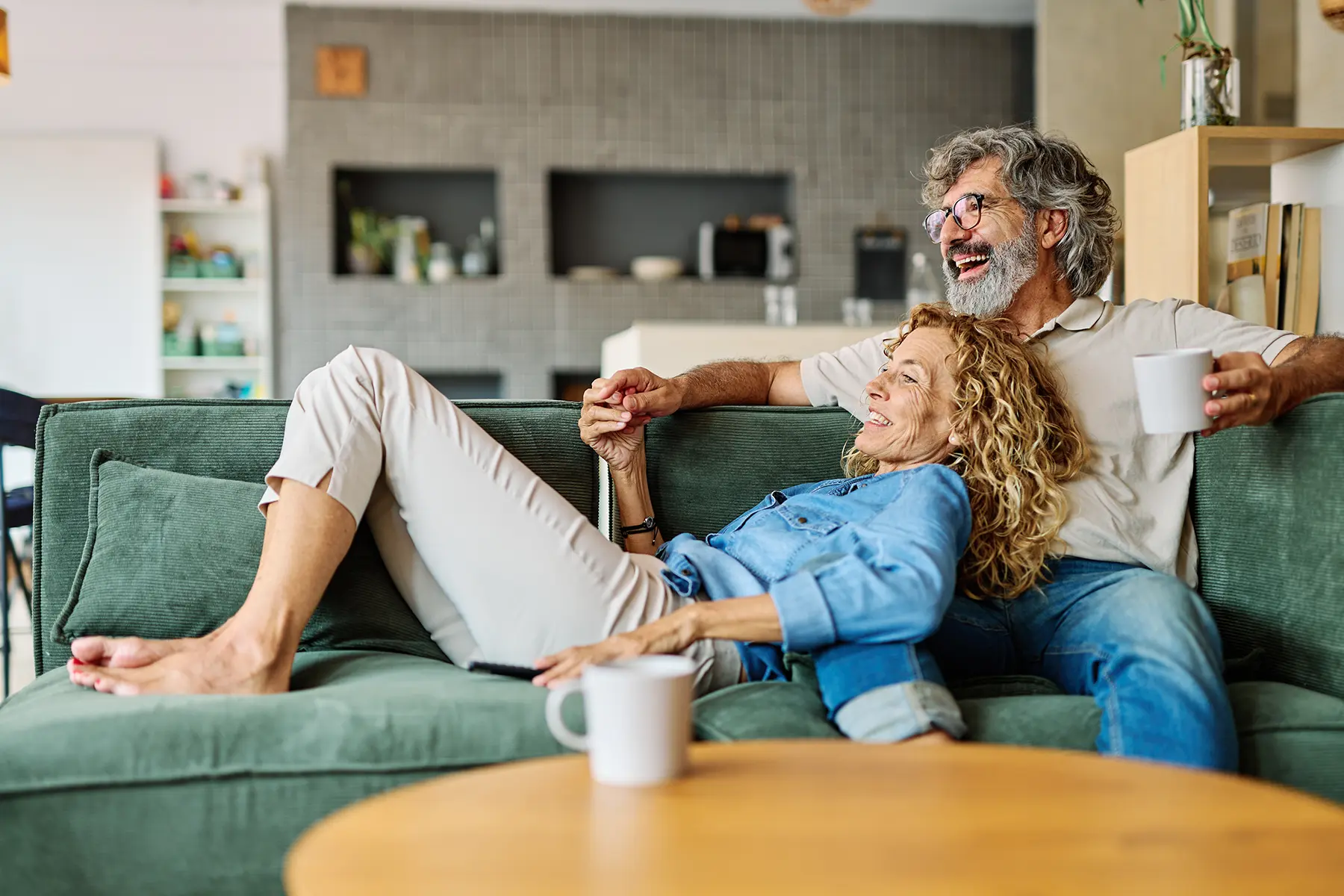 Happy middle aged couple having a laugh while cuddling on couch.