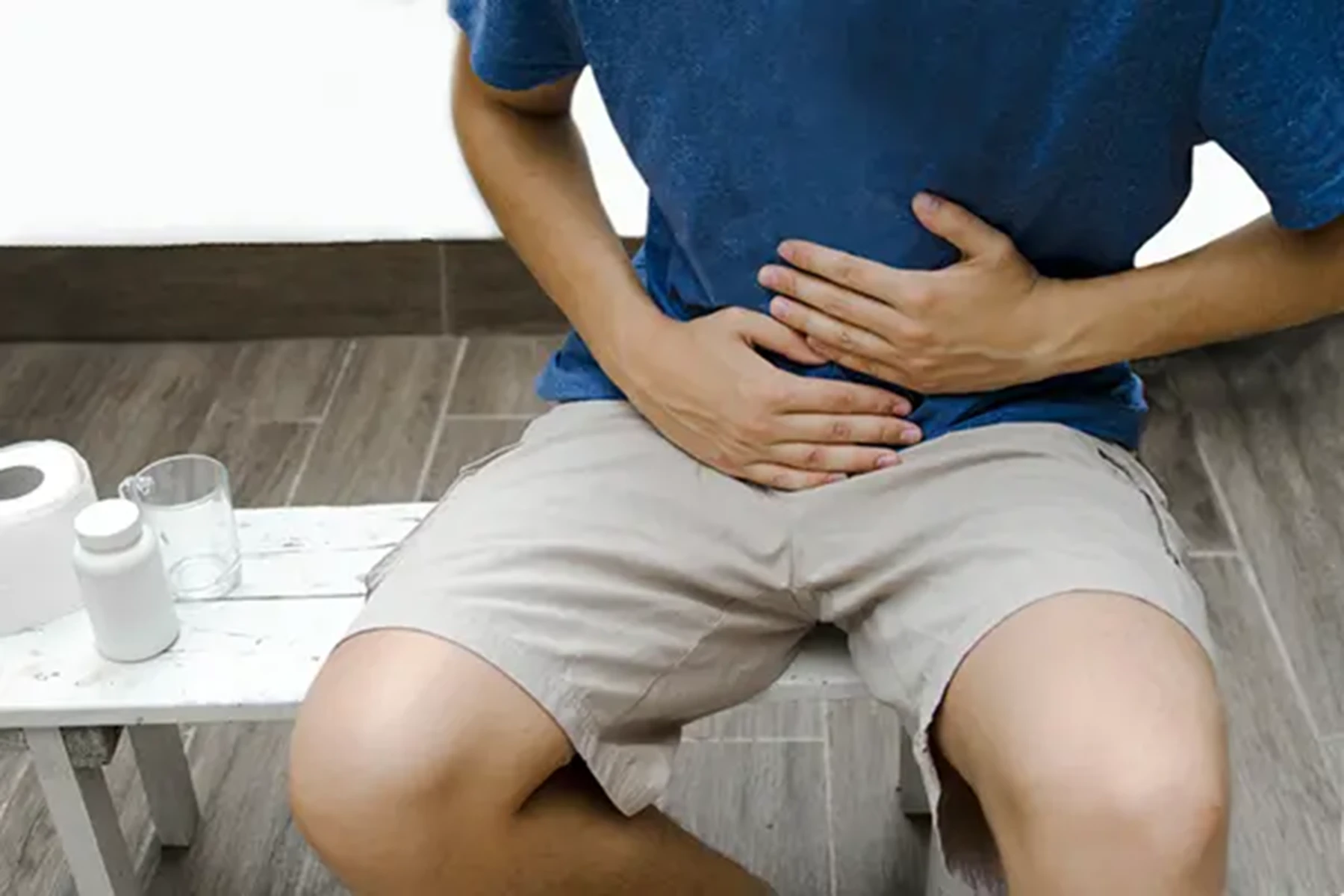 A man in a blue shirt sits on a bench and holds his abdomen.