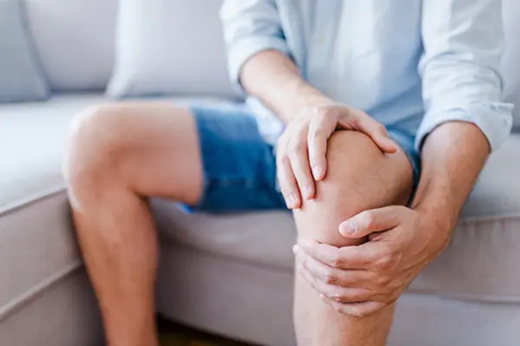 A close-up of a young man's hands on his knees. Although the man's face is not in the frame, it's fairly clear his knee is causing him pain. 