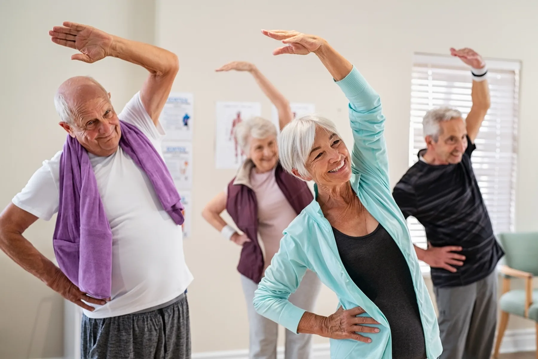 Four older people stretching with one hand on their hips and the other raised over their bodies.