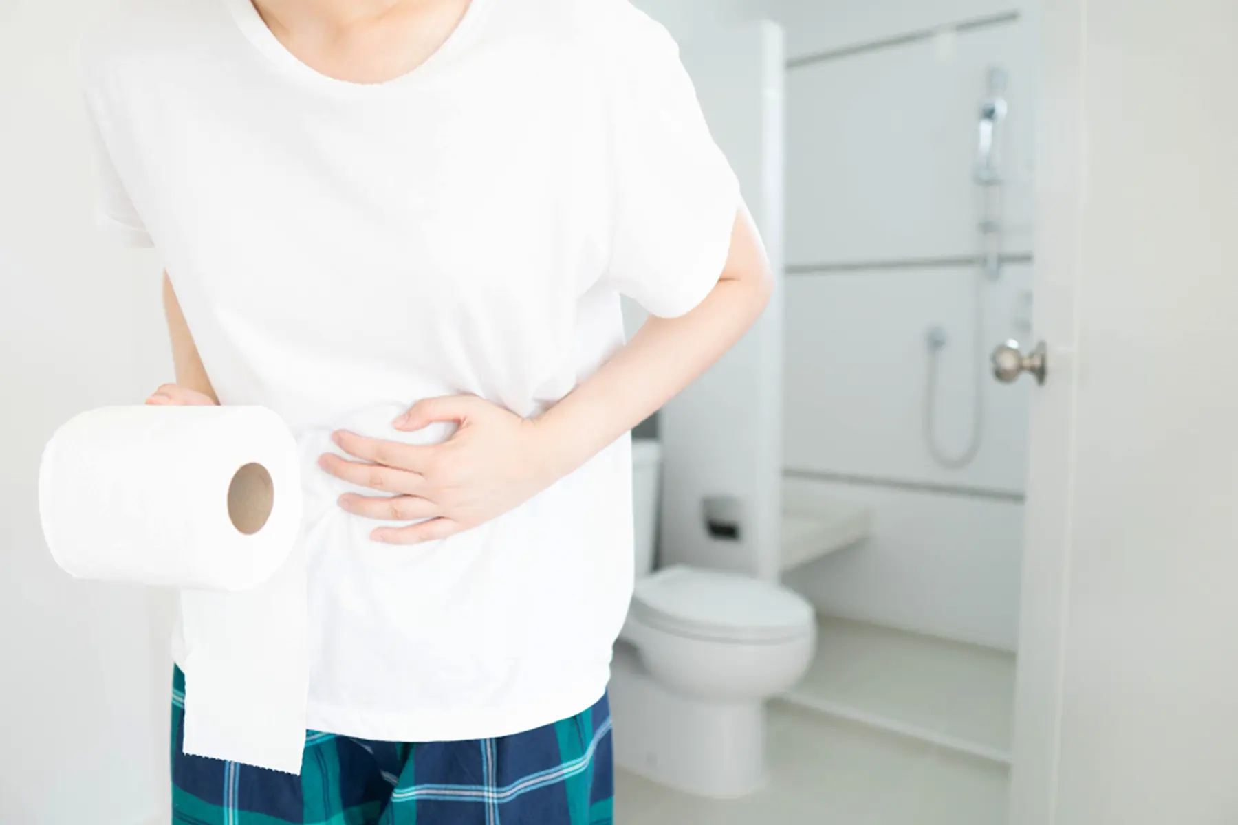 A person in a bathroom clutches their stomach with one hand and holds toilet paper in the other hand.