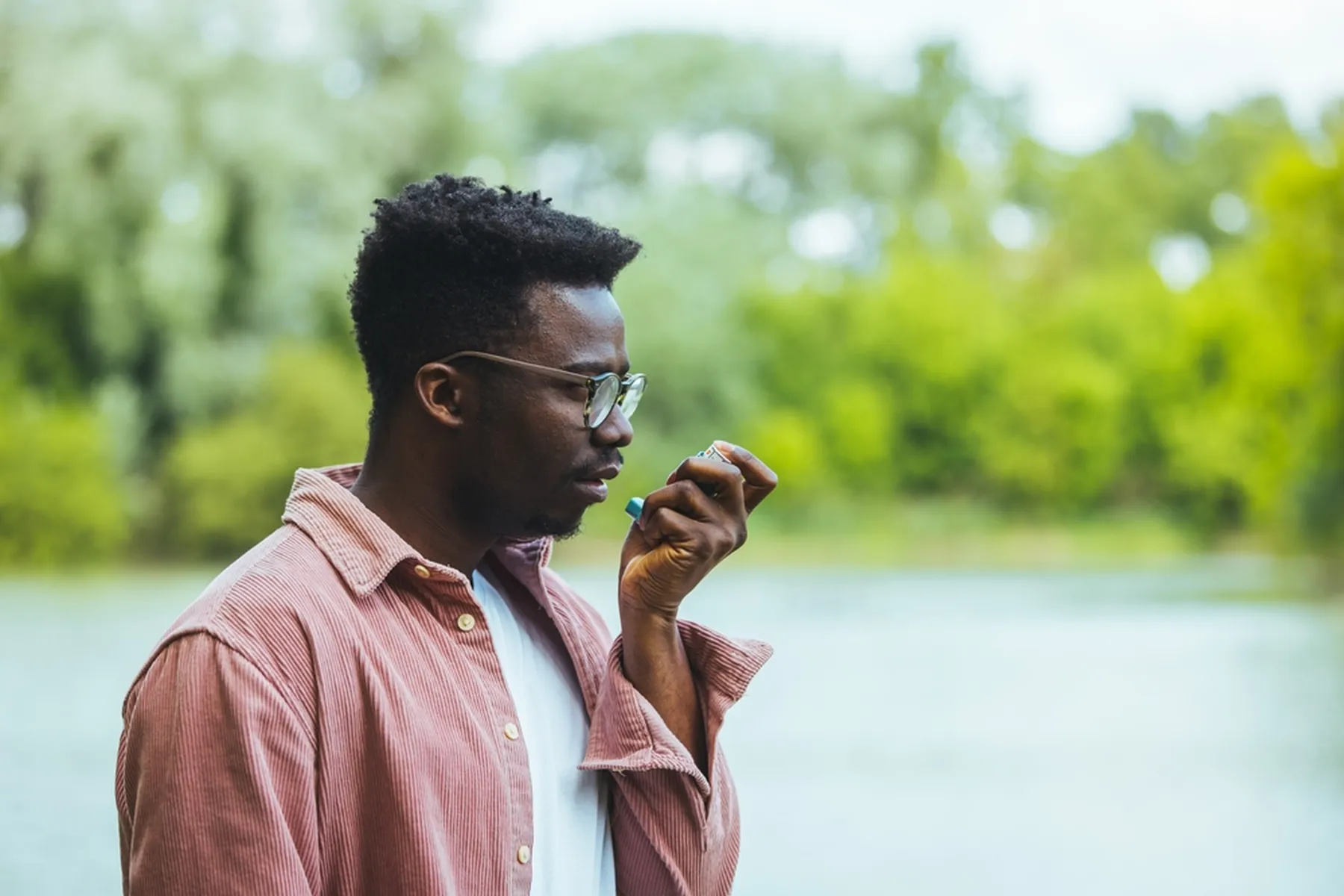 A man stands outside and uses an inhaler.