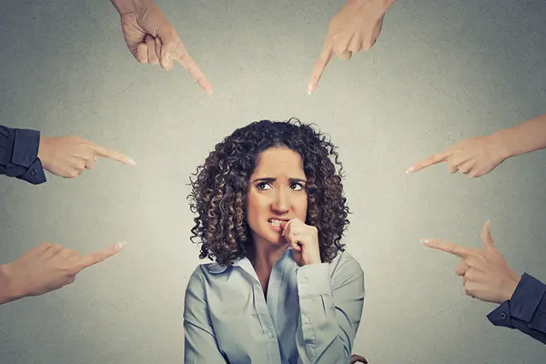 Woman biting her nail with anxious look on her face with fingers pointing at her surround her.