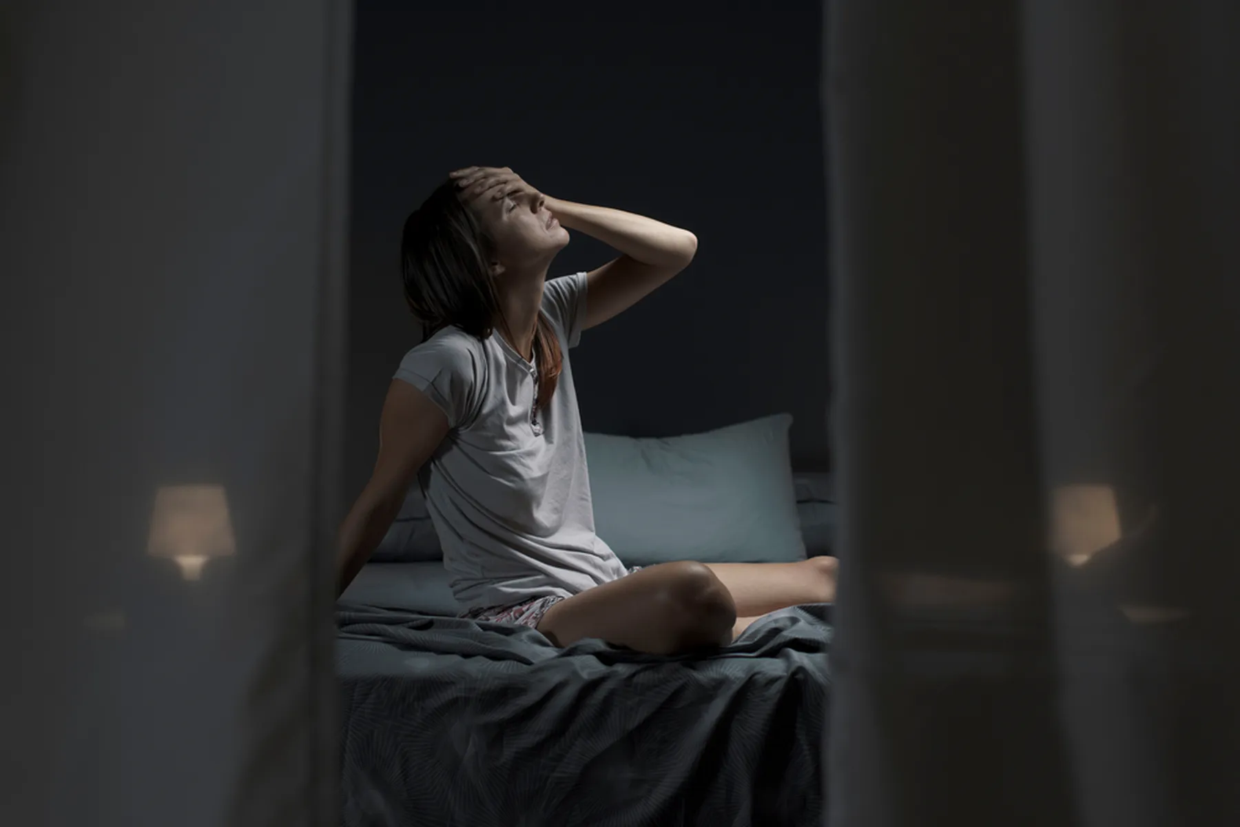 A woman sitting up in bed, drenched in sweat. One hand is on her head, and her eyes are closed. 