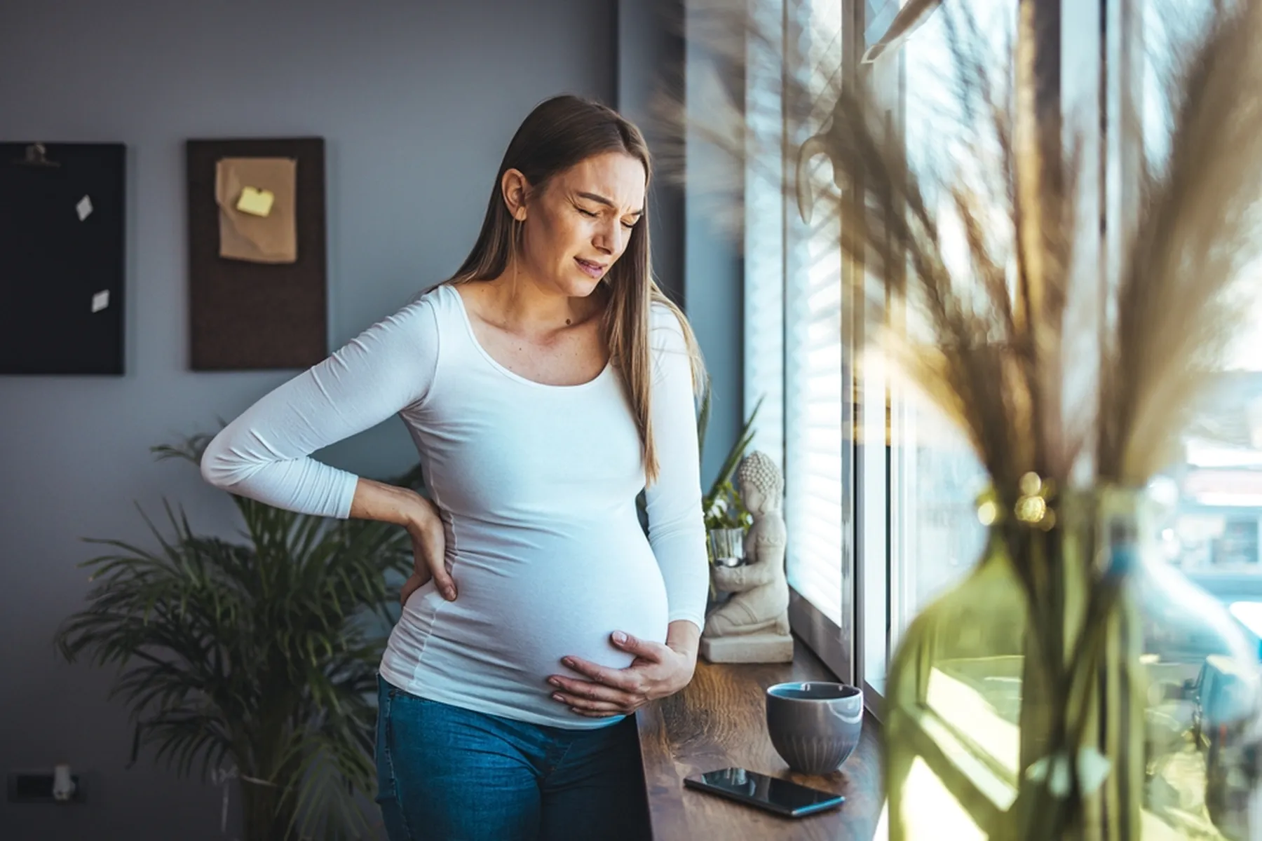 Pregnant woman holds her stomach and makes a pained face while also holding her back.